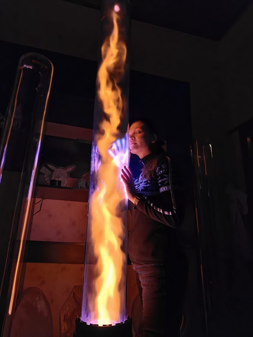 A person beside a full-height plasma tube, orange filaments climbing the column