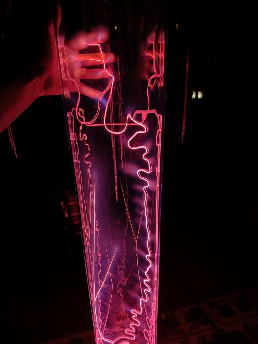 A hand pressed to a plasma tube, filaments reaching toward it